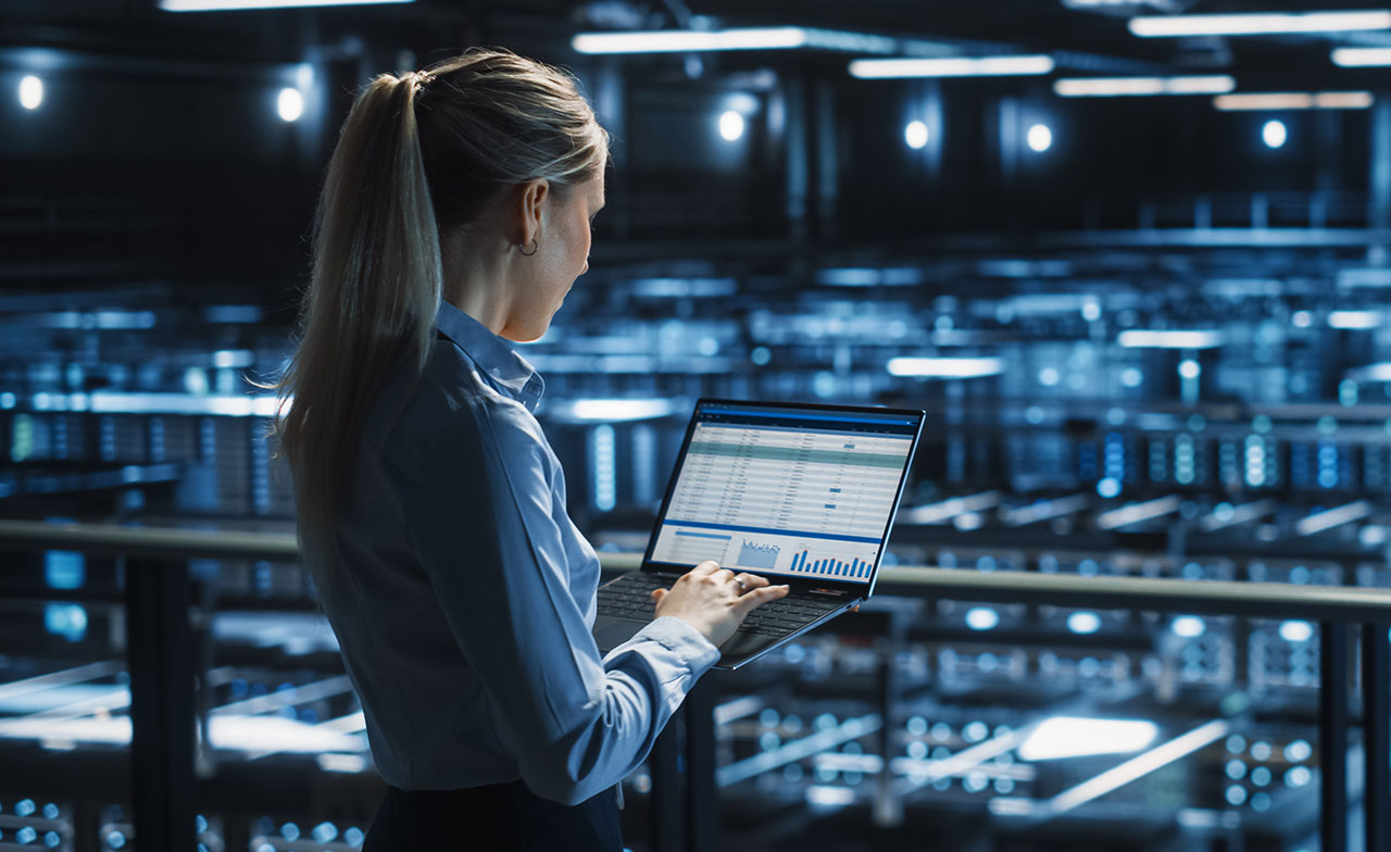 Consultant reviewing CGI SiteReliability360 on a laptop overlooking a server room Consultant reviewing CGI SiteReliability360 on a laptop overlooking a server room