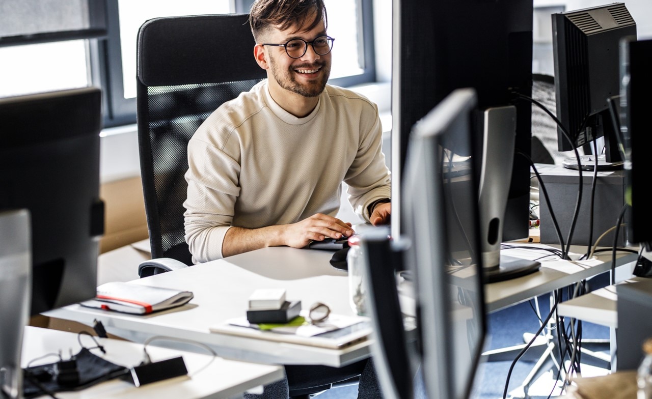 smiling-person-sitting-at-computer-desk A smiling person sitting at a computer desk
