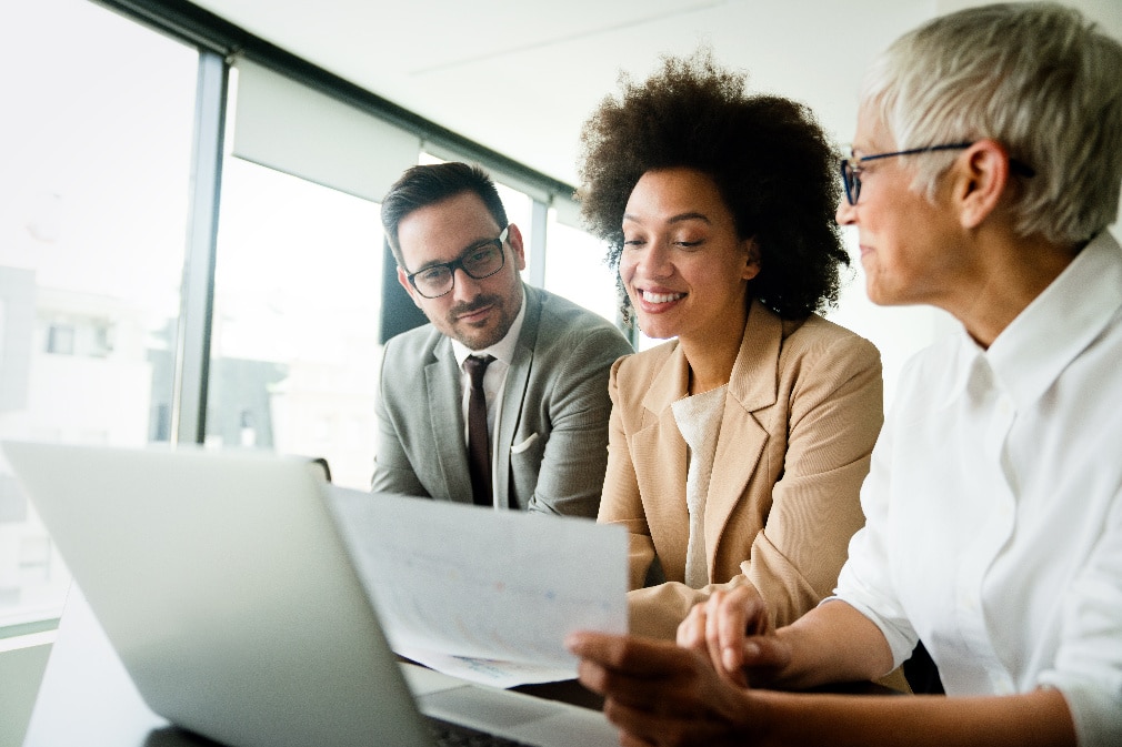 Trois professionnels examinent des données sur un document et un ordinateur portable Trois professionnels examinent des données sur un document et un ordinateur portable