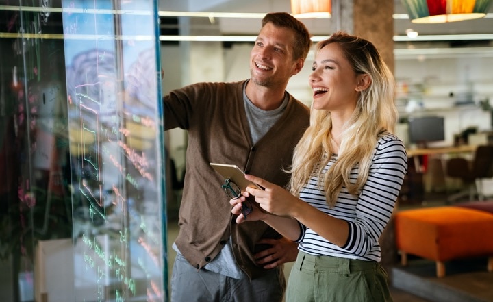 Zwei Personen stehen in einem modernen Büro und lachen zusammen