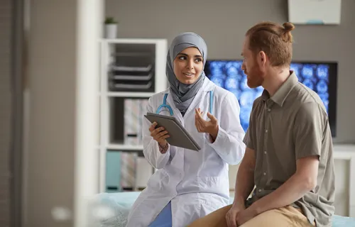 Male patient listening to his doctor while she telling about the disease using digital tablet…