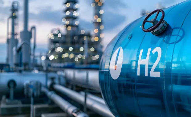 Hydrogen storage tank at an industrial site with pipelines and refinery in the background.