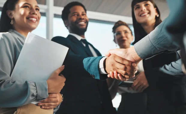 Four professionals smiling and shaking a client’s hand