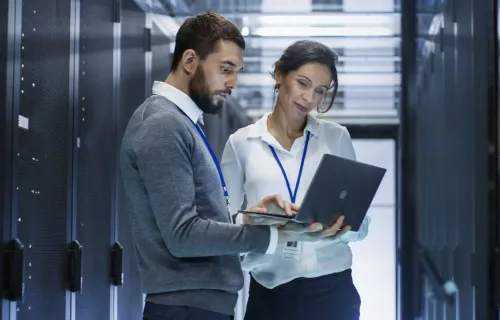 Consultants working in on a laptop in a server room discussing CGI SiteReliability360