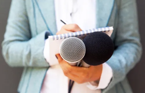 Journalist holding a microphone and writing on a notepad at news conference