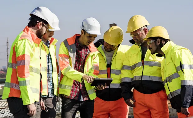 Group of workers in high vis jackets and hard hats look at tablet at wastewater plant