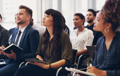 Training session with audience of professionals sitting in chairs holding notebooks