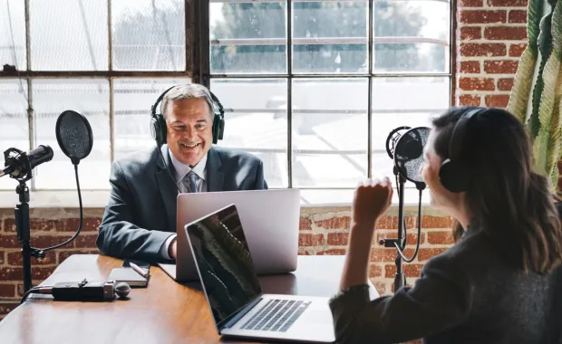 Two broadcasters speaking in front of laptops and microphones
