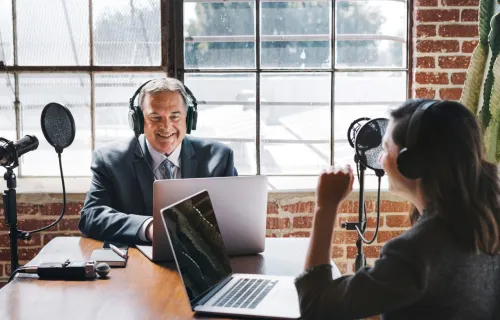 Two broadcasters speaking in front of laptops and microphones