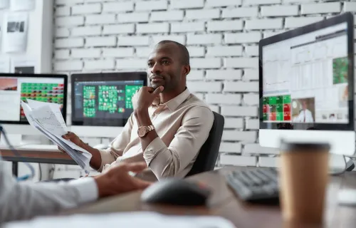 Two trade finance colleagues discussing ideas while sitting in front of multiple computer…